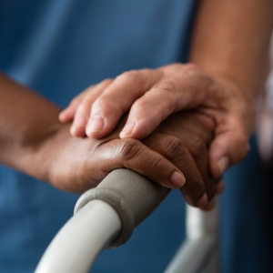 Cropped hands of nurse and senior woman holding walker in nursing home